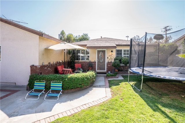 back of house featuring a trampoline, a lawn, and a patio area