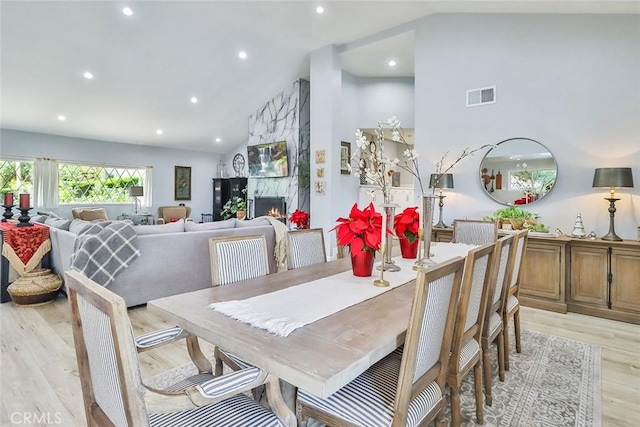 dining space featuring a fireplace, high vaulted ceiling, and light hardwood / wood-style flooring