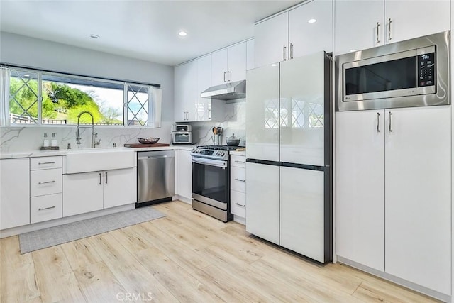 kitchen with under cabinet range hood, a sink, light countertops, appliances with stainless steel finishes, and light wood finished floors