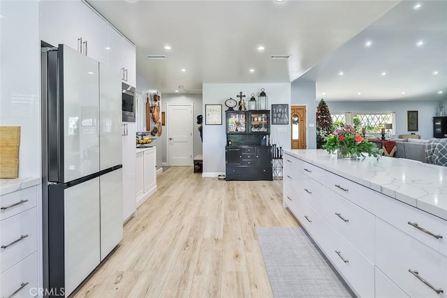 kitchen with light stone countertops, white fridge, white cabinets, and light hardwood / wood-style flooring