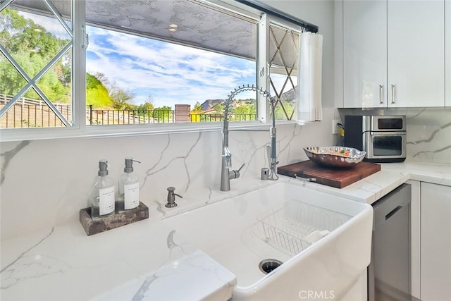 kitchen featuring tasteful backsplash, light stone countertops, sink, and white cabinets