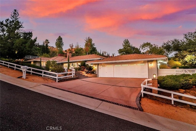 view of front facade featuring driveway, a garage, a tile roof, a fenced front yard, and stucco siding