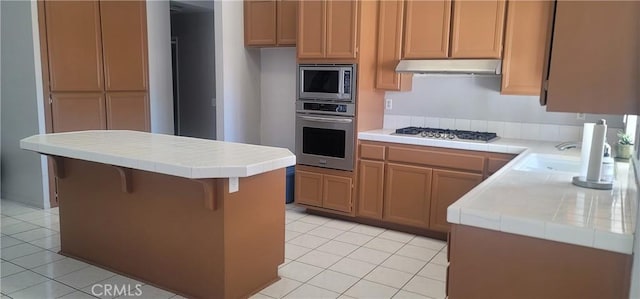 kitchen featuring appliances with stainless steel finishes, sink, light tile patterned floors, a center island, and tile countertops