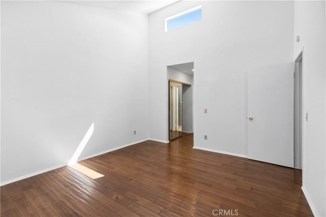 spare room with a towering ceiling and dark wood-type flooring