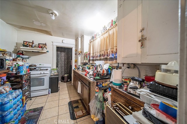 kitchen featuring white range with gas cooktop, light tile patterned floors, and white cabinets