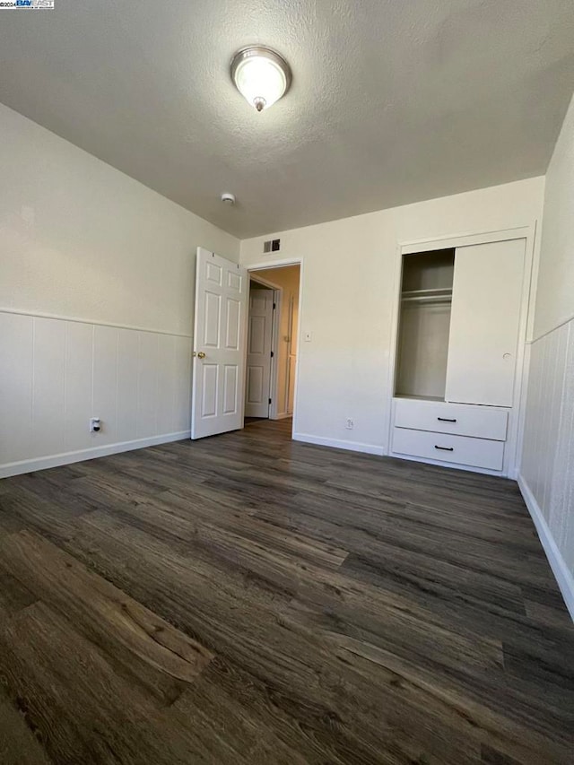 unfurnished bedroom featuring a textured ceiling, dark wood-type flooring, and a closet