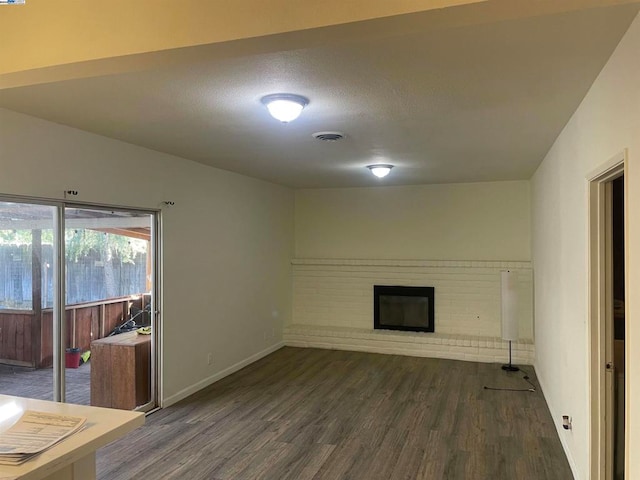 unfurnished living room featuring a brick fireplace and dark wood-type flooring