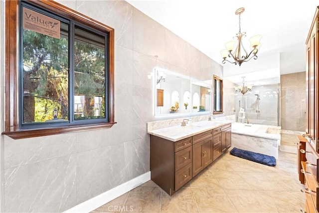 bathroom with an inviting chandelier, tiled tub, tile patterned flooring, tile walls, and vanity