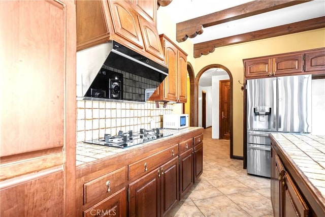 kitchen featuring tile counters, backsplash, stainless steel fridge with ice dispenser, and gas stovetop