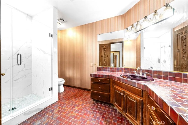 bathroom with toilet, vanity, tile patterned floors, wooden walls, and a shower with shower door