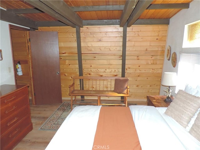 bedroom featuring light hardwood / wood-style flooring, beamed ceiling, and wood walls