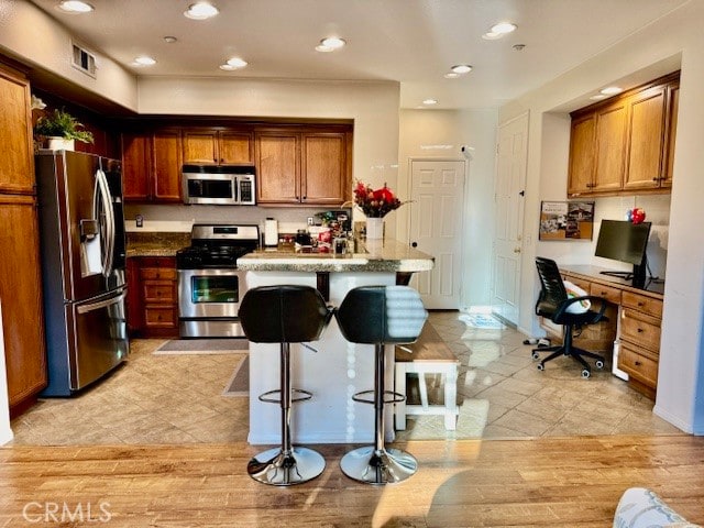 kitchen featuring a kitchen island, built in desk, light hardwood / wood-style flooring, stainless steel appliances, and a breakfast bar