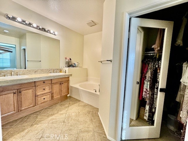 bathroom with vanity, a textured ceiling, and tiled bath