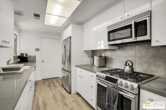 kitchen featuring decorative backsplash, white cabinetry, light hardwood / wood-style floors, and appliances with stainless steel finishes