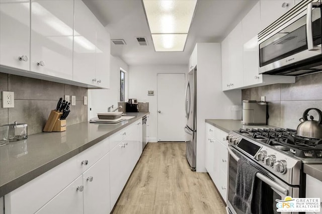 kitchen with white cabinets, appliances with stainless steel finishes, light wood-type flooring, and decorative backsplash