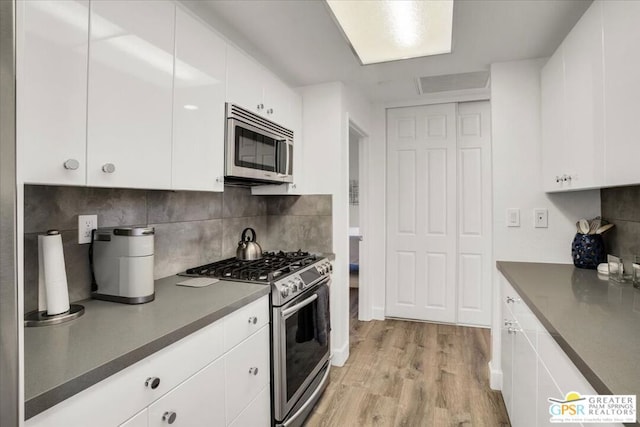 kitchen with white cabinets, decorative backsplash, light hardwood / wood-style floors, and stainless steel appliances