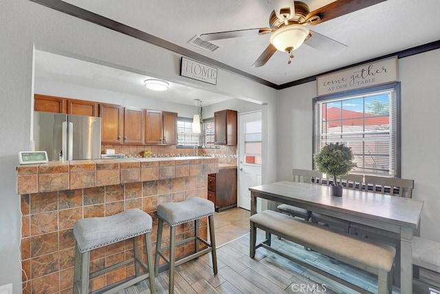 kitchen featuring hanging light fixtures, tasteful backsplash, kitchen peninsula, stainless steel fridge, and light hardwood / wood-style floors