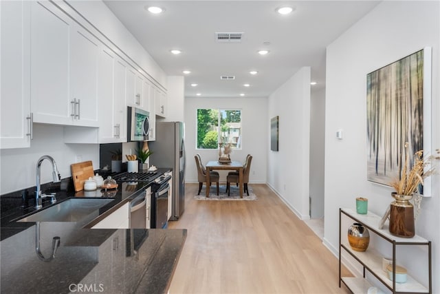 kitchen with sink, stainless steel appliances, dark stone counters, white cabinets, and light wood-type flooring