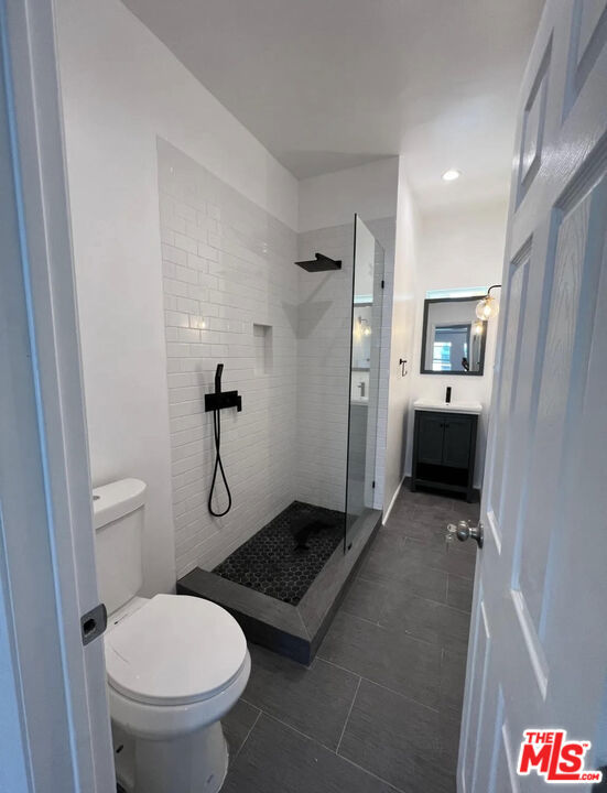 bathroom with a tile shower, tile patterned flooring, vanity, and toilet