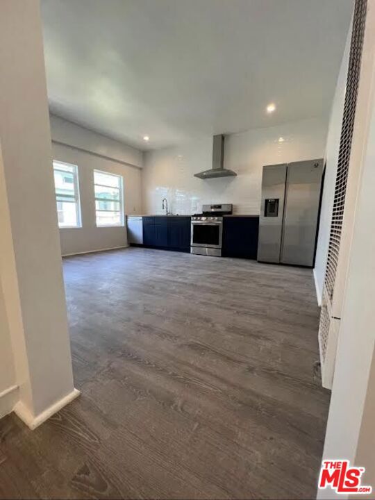 kitchen featuring appliances with stainless steel finishes, dark hardwood / wood-style floors, wall chimney range hood, and sink