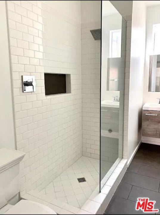 bathroom featuring vanity, tile patterned flooring, toilet, and tiled shower