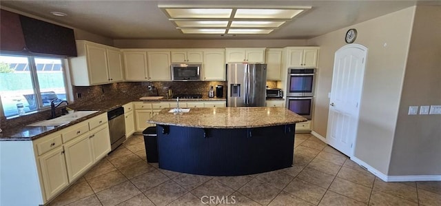 kitchen featuring a sink, a kitchen island, stainless steel appliances, dark stone counters, and decorative backsplash