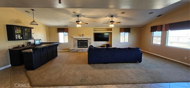 tiled living room featuring vaulted ceiling, a stone fireplace, visible vents, and carpet floors