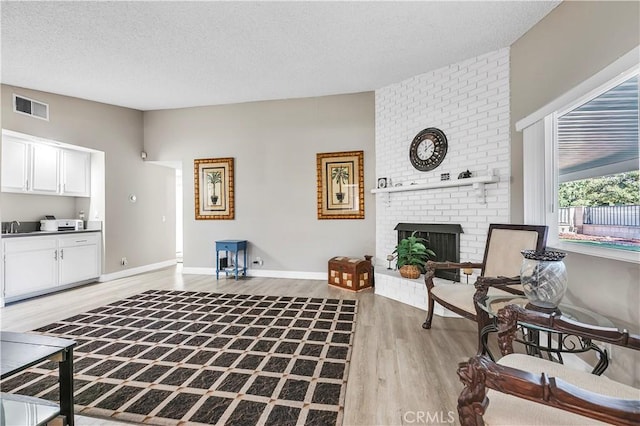 living room with light wood-type flooring, a textured ceiling, and a brick fireplace