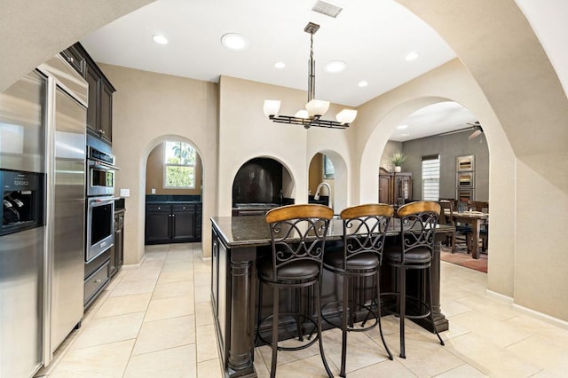 kitchen featuring a kitchen bar, light tile patterned floors, a center island with sink, dark stone countertops, and hanging light fixtures