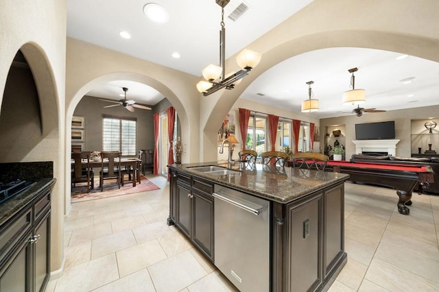 kitchen with sink, dishwasher, hanging light fixtures, dark stone countertops, and a kitchen island with sink