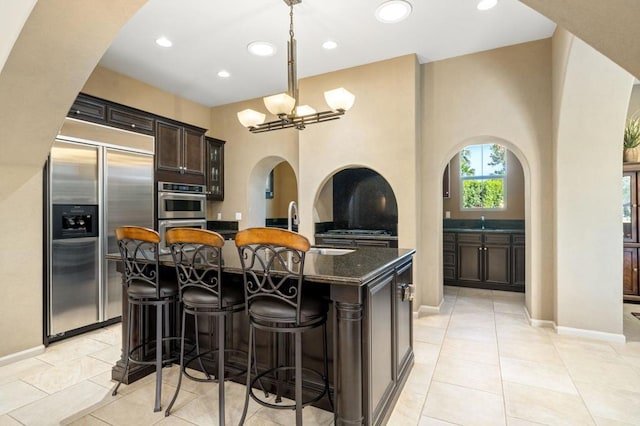 kitchen with a center island, a kitchen breakfast bar, dark stone counters, dark brown cabinets, and appliances with stainless steel finishes