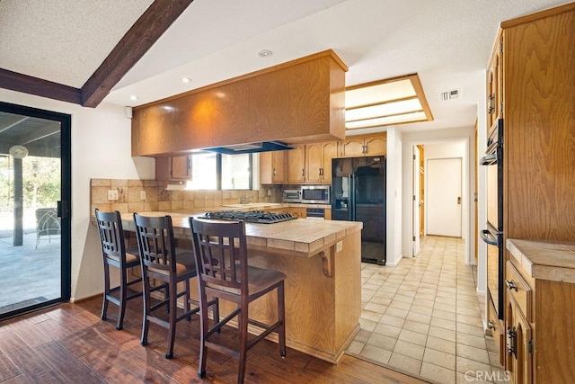 kitchen featuring kitchen peninsula, backsplash, beam ceiling, a breakfast bar, and black appliances