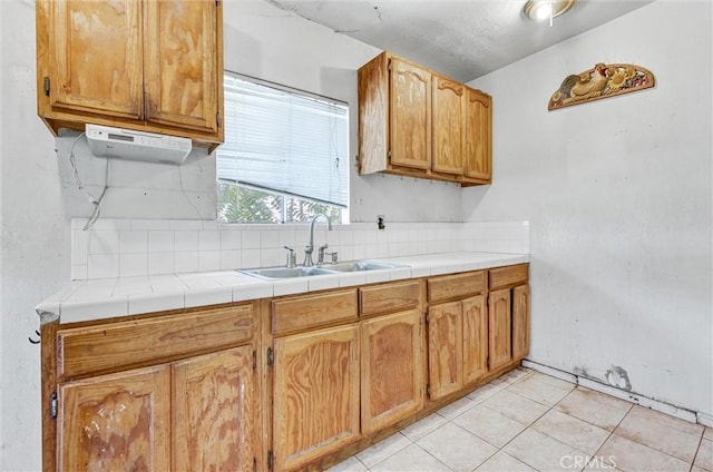 kitchen with tile counters, light tile patterned floors, sink, and tasteful backsplash