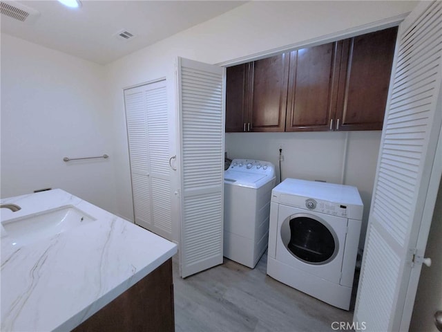 laundry room featuring cabinets, sink, light hardwood / wood-style floors, and washing machine and clothes dryer