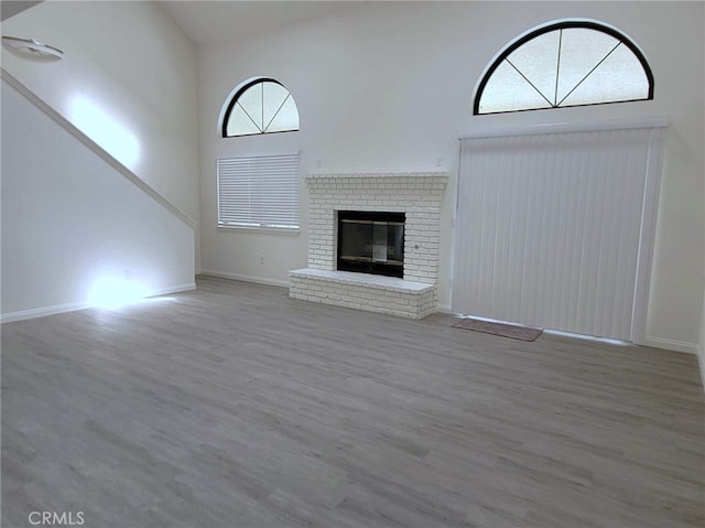 unfurnished living room featuring wood-type flooring, a brick fireplace, and high vaulted ceiling