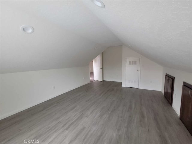 bonus room with lofted ceiling, dark hardwood / wood-style floors, and a textured ceiling