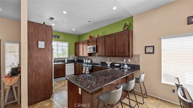 kitchen featuring dark stone counters, kitchen peninsula, a kitchen breakfast bar, decorative backsplash, and appliances with stainless steel finishes