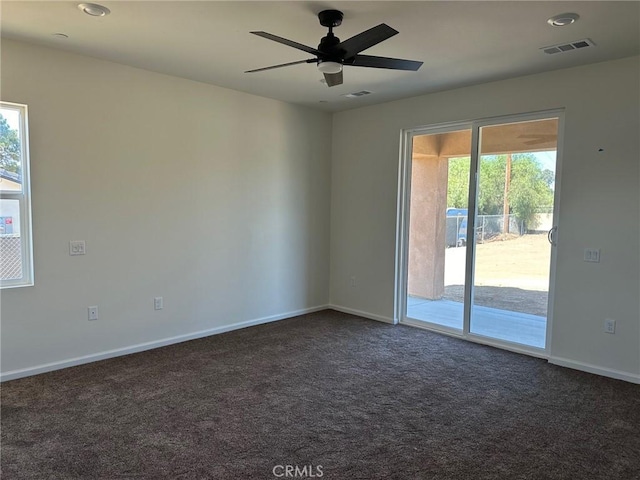 spare room with dark carpet, ceiling fan, and a healthy amount of sunlight