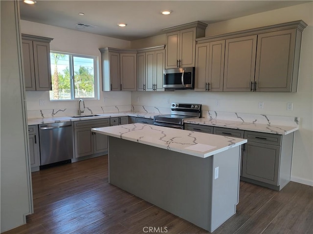 kitchen with gray cabinetry, sink, dark wood-type flooring, stainless steel appliances, and a kitchen island