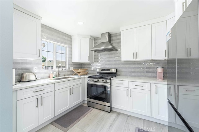 kitchen featuring wall chimney exhaust hood, stainless steel gas stove, sink, and white cabinetry