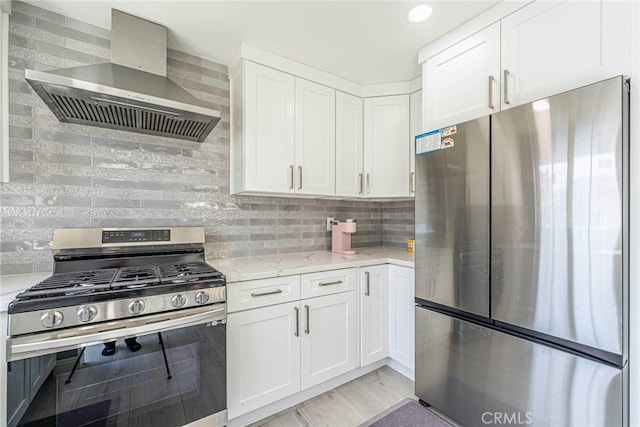 kitchen featuring appliances with stainless steel finishes, white cabinetry, wall chimney range hood, and light stone counters