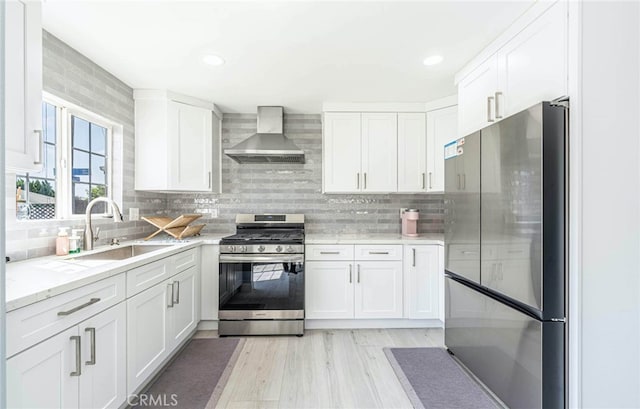 kitchen with white cabinets, appliances with stainless steel finishes, sink, and wall chimney range hood