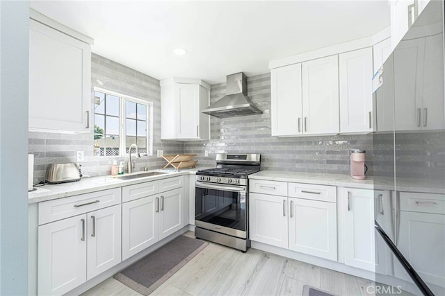 kitchen with wall chimney exhaust hood, white cabinets, gas stove, and sink