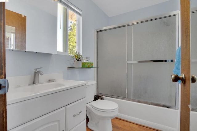 full bathroom with wood-type flooring, vanity, combined bath / shower with glass door, and toilet