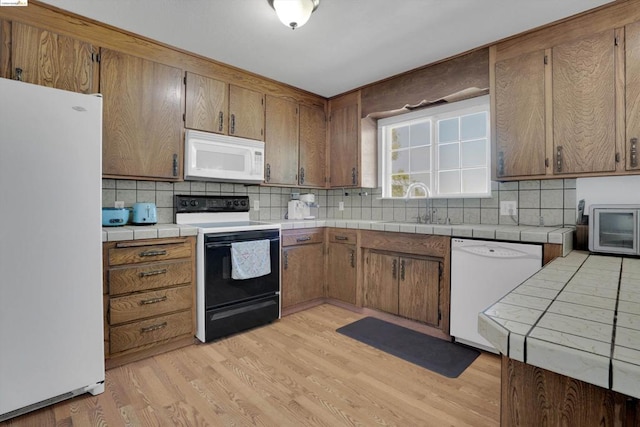 kitchen featuring white appliances, sink, tile countertops, and light hardwood / wood-style flooring