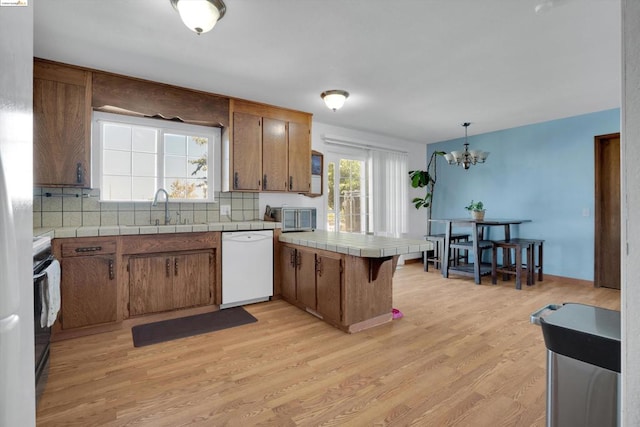 kitchen featuring light hardwood / wood-style floors, kitchen peninsula, a notable chandelier, white dishwasher, and tile countertops