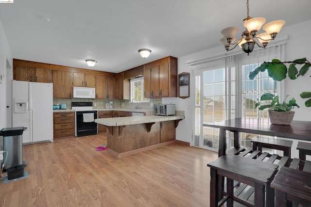 kitchen with white appliances, decorative light fixtures, light hardwood / wood-style flooring, and tile counters