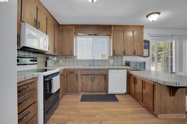 kitchen with sink, kitchen peninsula, white appliances, light hardwood / wood-style flooring, and backsplash