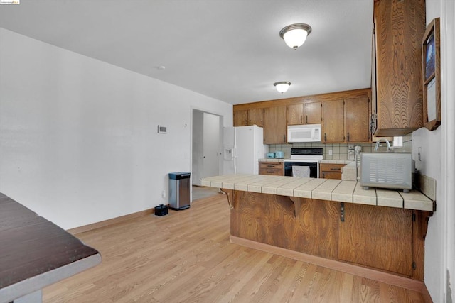 kitchen featuring kitchen peninsula, light wood-type flooring, white appliances, and tile countertops