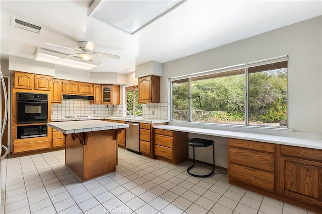 kitchen with ceiling fan, tile counters, stainless steel dishwasher, decorative backsplash, and a kitchen island